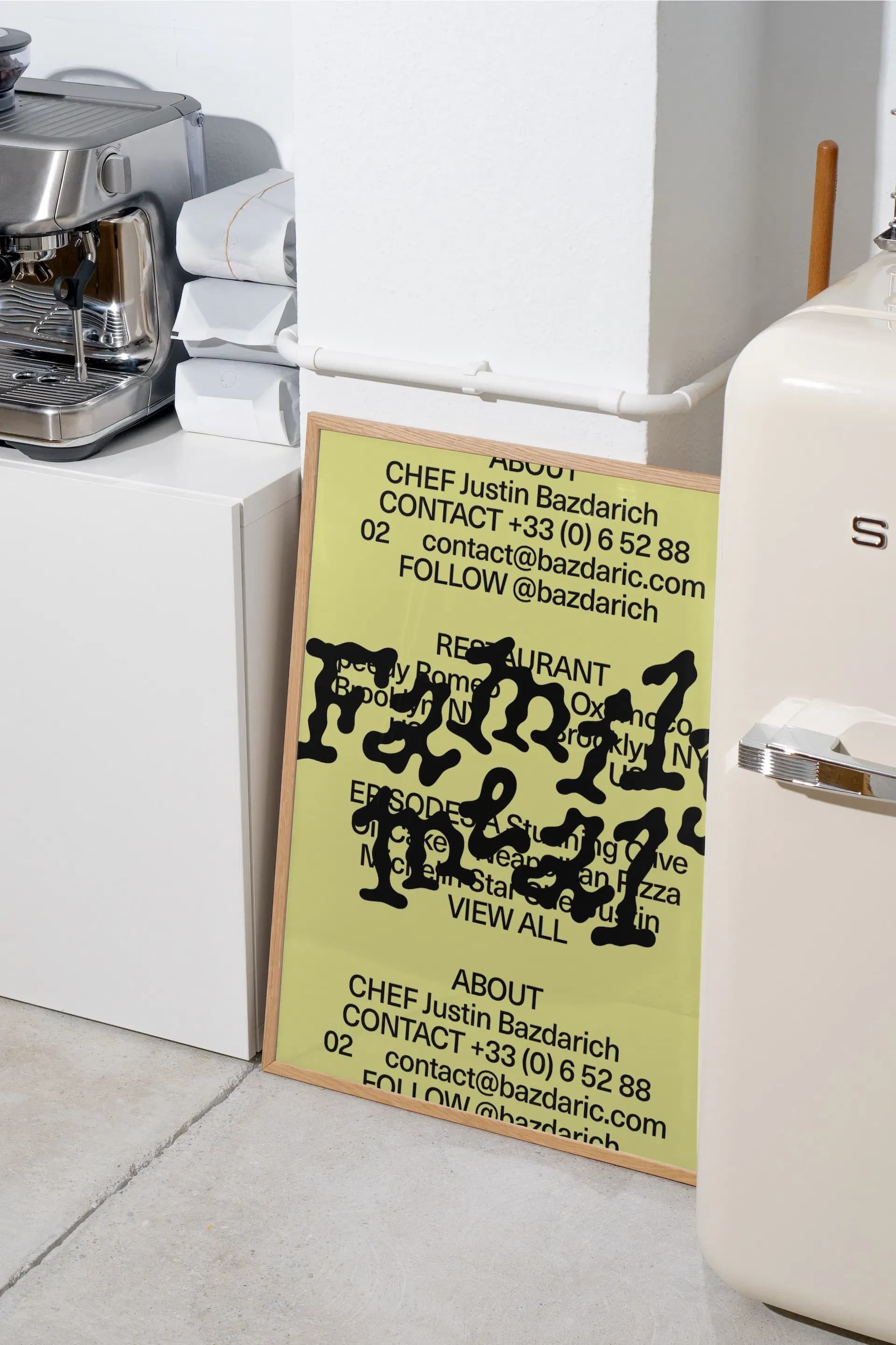 Yellow typography poster from Bazdarich Productions standing in a kitchen between a fridge and coffee machine