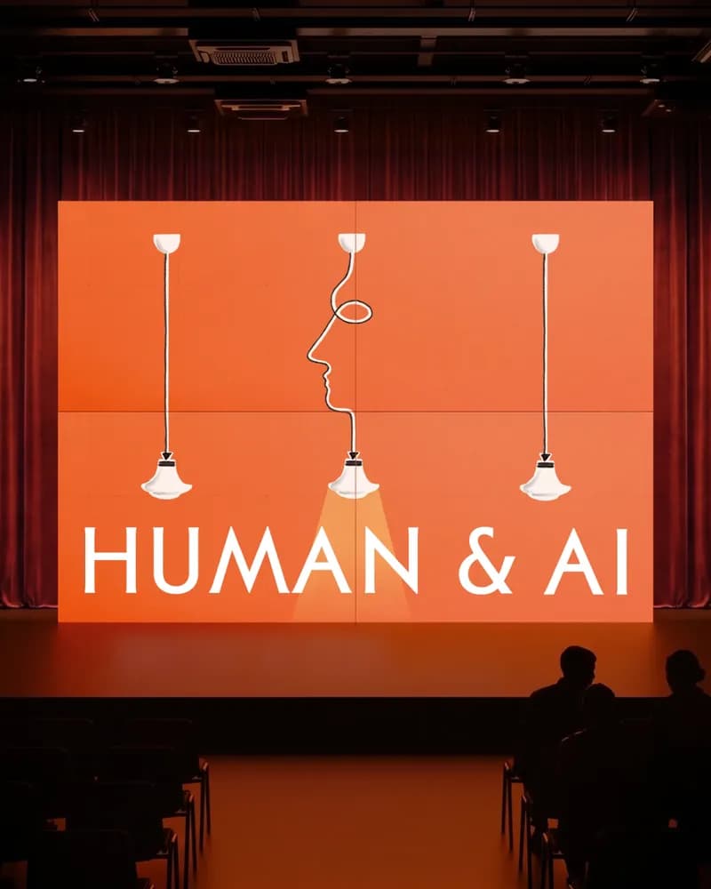 Auditorium stage with an orange screen reading 'Human & AI' in white capitals. Drawn pendant lamps surround a line-drawn face profile. The audience appears as silhouettes.