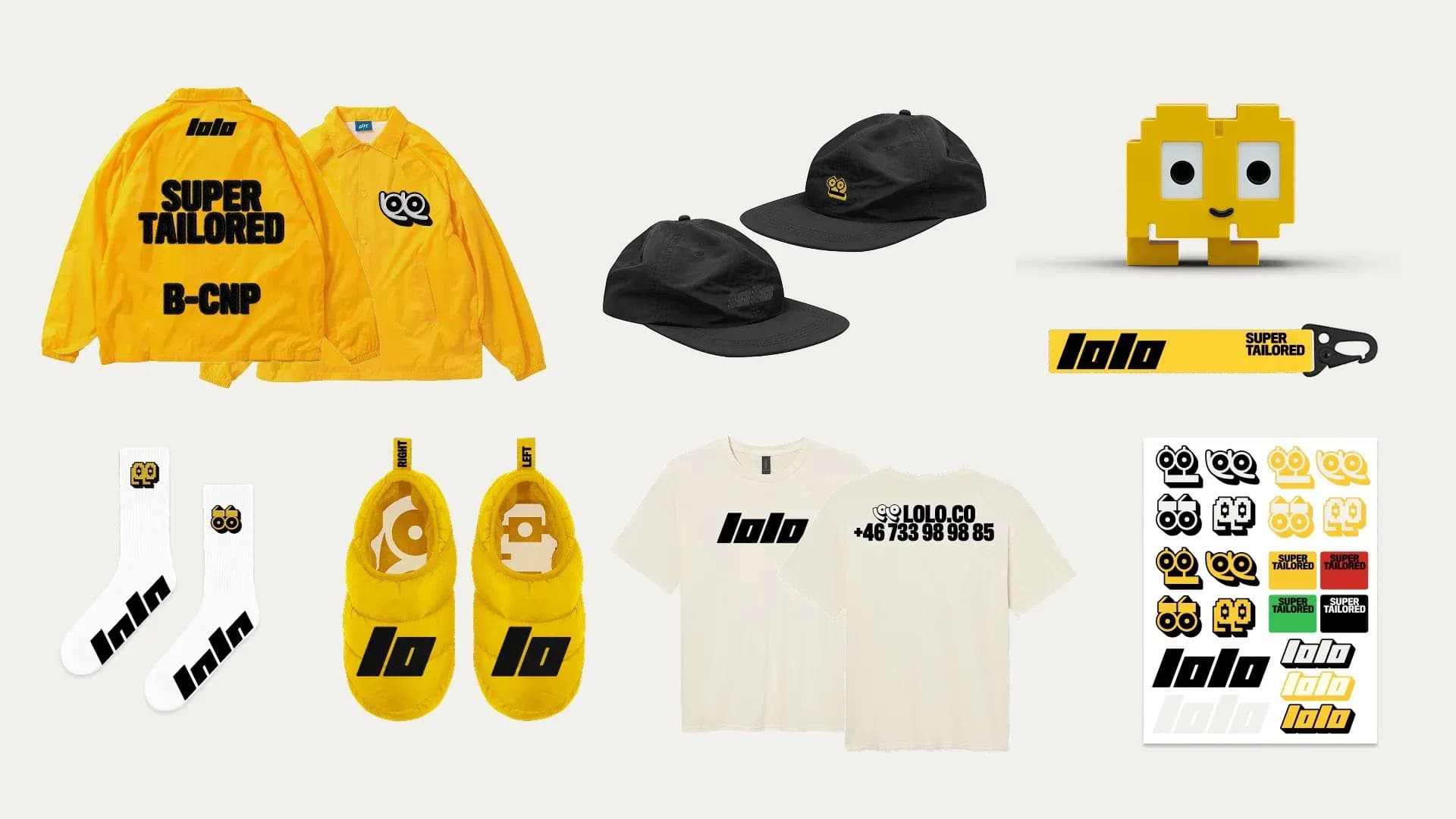 Flat lay of Lolo's merchandise collection: yellow jackets, black caps, pixelated mascot figure, lanyard, white socks, yellow slippers, t-shirts, and sticker sheets – all in the brand's yellow-black-white palette.