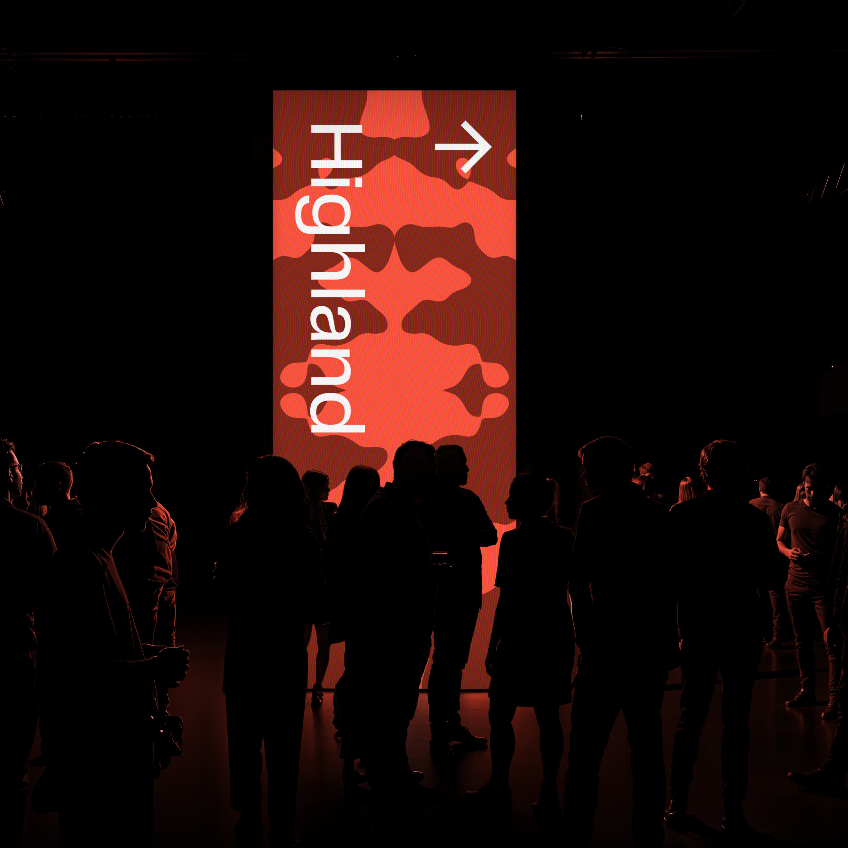 Event photo: tall vertical LED screen glowing in a dark festival venue displaying 'Highland →' in white on the brand's red organic blob pattern, surrounded by silhouetted festival-goers.