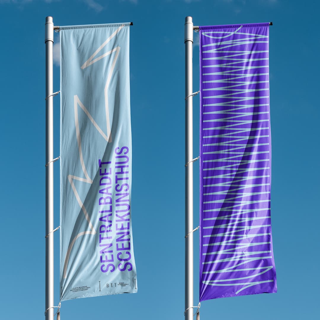Two banner flags against a blue sky: the left light blue with abstract line drawings and 'Sentralbadet Scenekunsthus' in purple, the right violet with a light blue line pattern – from the new visual identity.