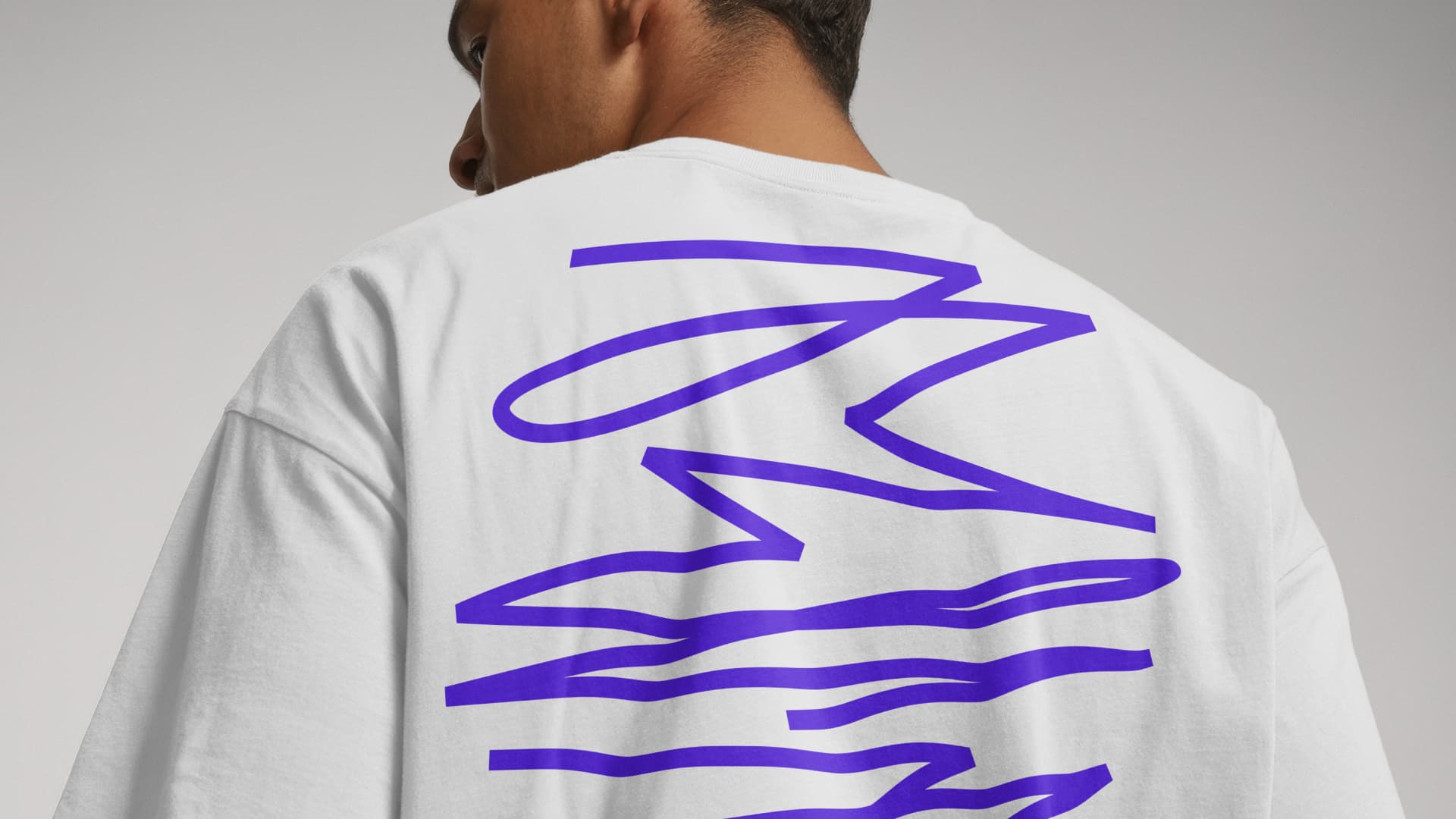 Close-up of a person wearing a white T-shirt with a large purple line-art print on the back – from the merchandise collection for Sentralbadet Scenekunsthus.