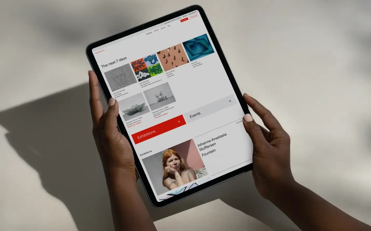 Person holding an iPad displaying Kunsthal Spritten's homepage with 'The next 7 days' section, exhibition grid, and upcoming events.