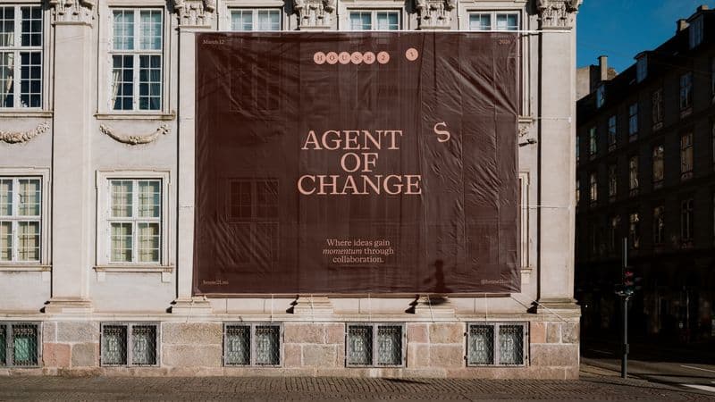 A-frame sidewalk sign announcing 'Agent of Change', a House21 event on March 12, 2026, with the tagline 'Where ideas gain momentum through collaboration'.