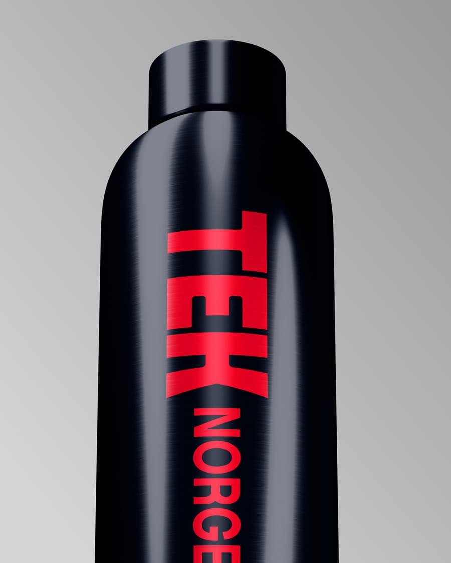Black metal water bottle with "TEK NORGE" printed vertically in large red letters against a grey background. Shows the brand's bold typography applied to merchandise.