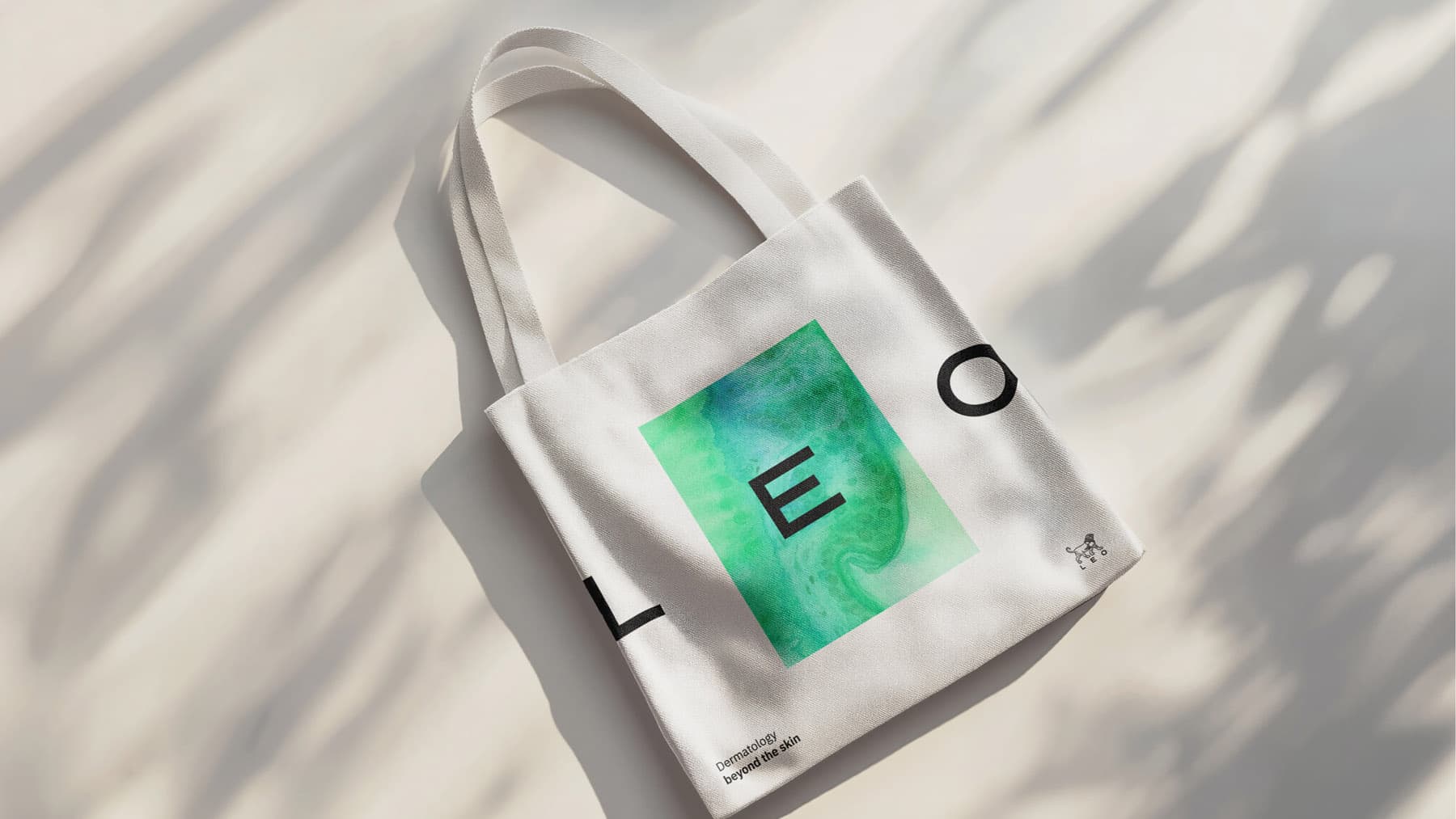 White canvas tote bag with LEO Pharma branding: Green watercolor graphic element, LEO logotype, and 'Dermatology beyond the skin' text.
