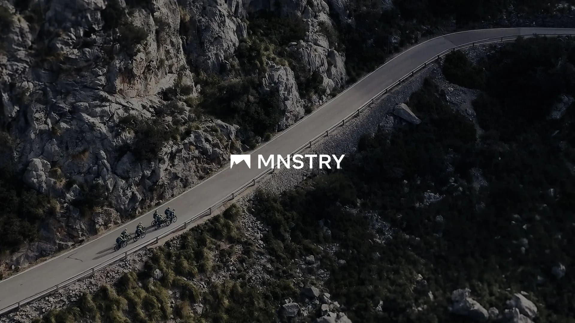 Cyclists riding op a mountain and the mnstry logo placed on top of the photograph