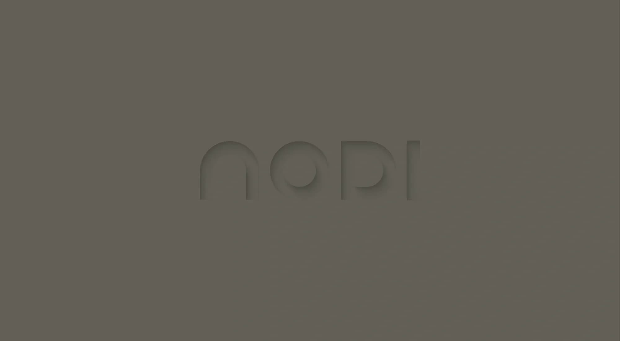 NODI logo in a rounded, geometric lowercase wordmark, embossed tone-on-tone into a warm grey surface. Soft shadow and light give the logo a subtle relief effect.
