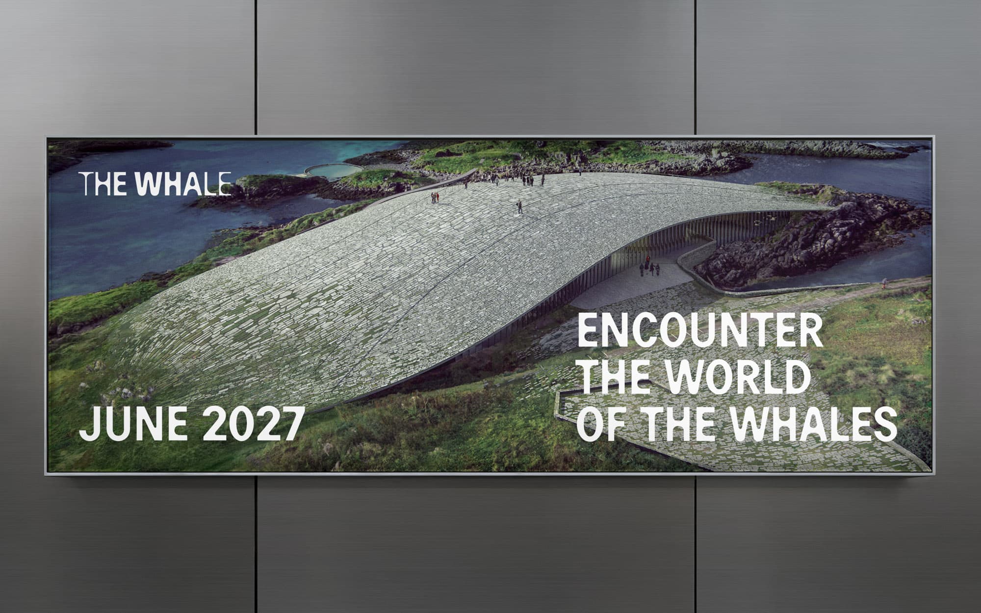 Outdoor advertising mockup: horizontal billboard on grey wall with aerial photo of The Whale building's whale-shaped roof on the Norwegian coastline. Copy: "Encounter the World of the Whales – June 2027".