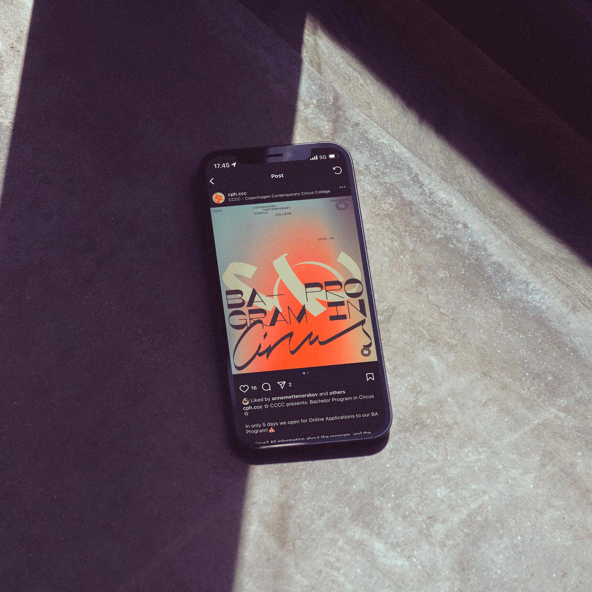 iPhone on a concrete floor shows CCCC's Instagram post announcing admissions for the Bachelor Program in Circus with orange gradient and custom typography.