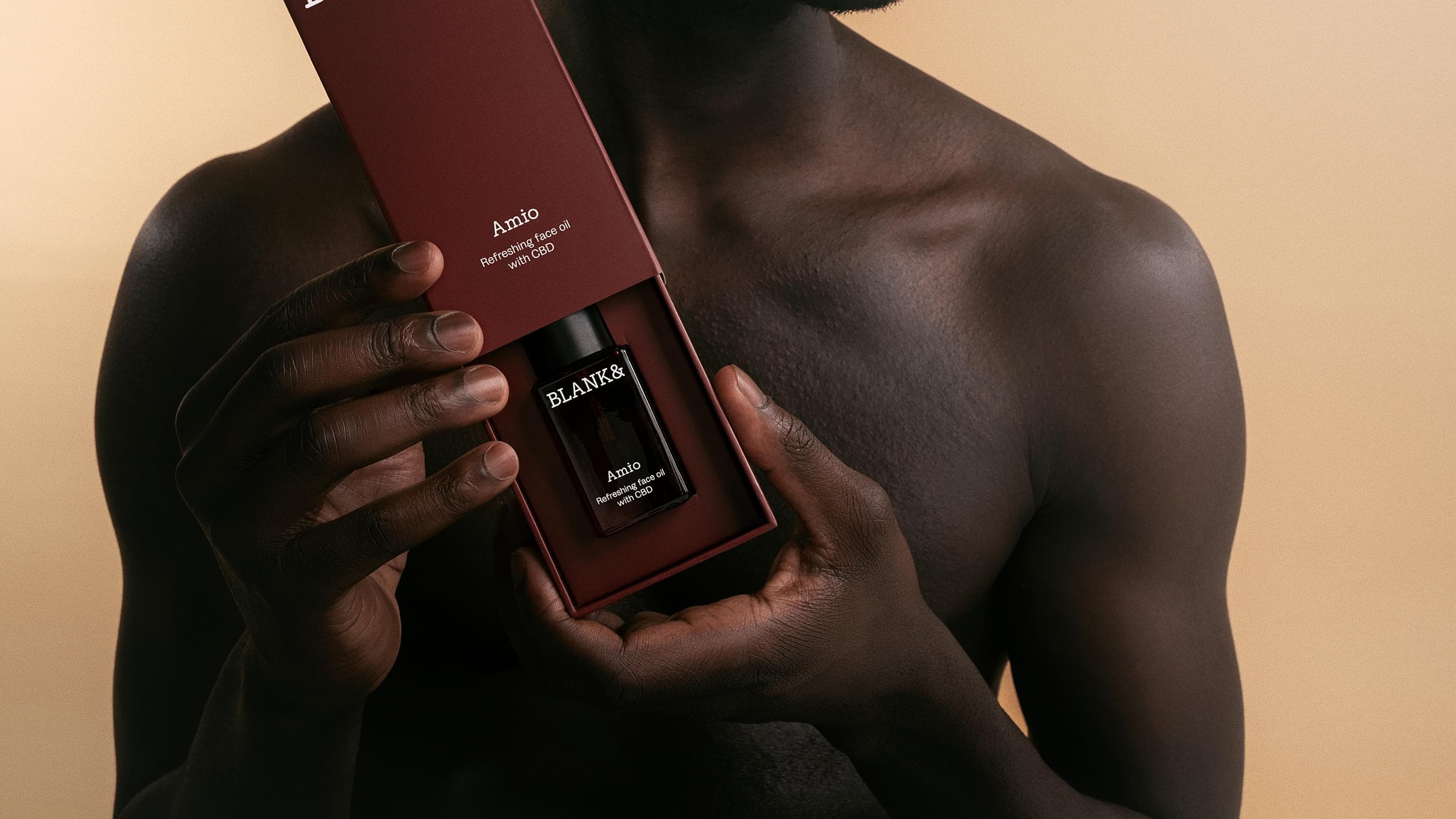 Blank& Amio hero image: man holds an open dark red box revealing the burgundy dropper bottle 'Amio – Refreshing face oil with CBD' against his bare chest.