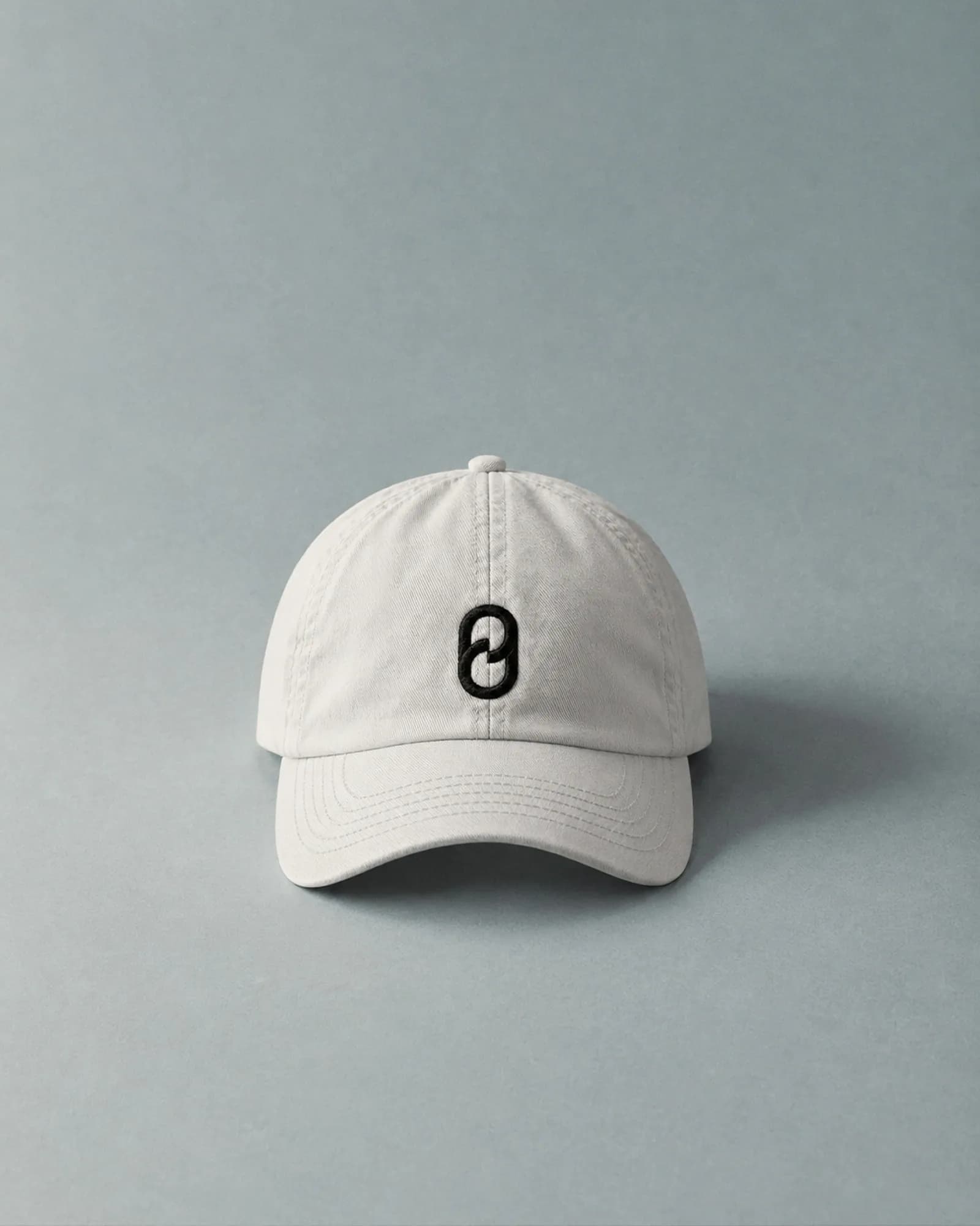 Off-white cap with the P/0 symbol embroidered on the front, photographed against a blue-grey background. The symbol is the only mark on the cap.