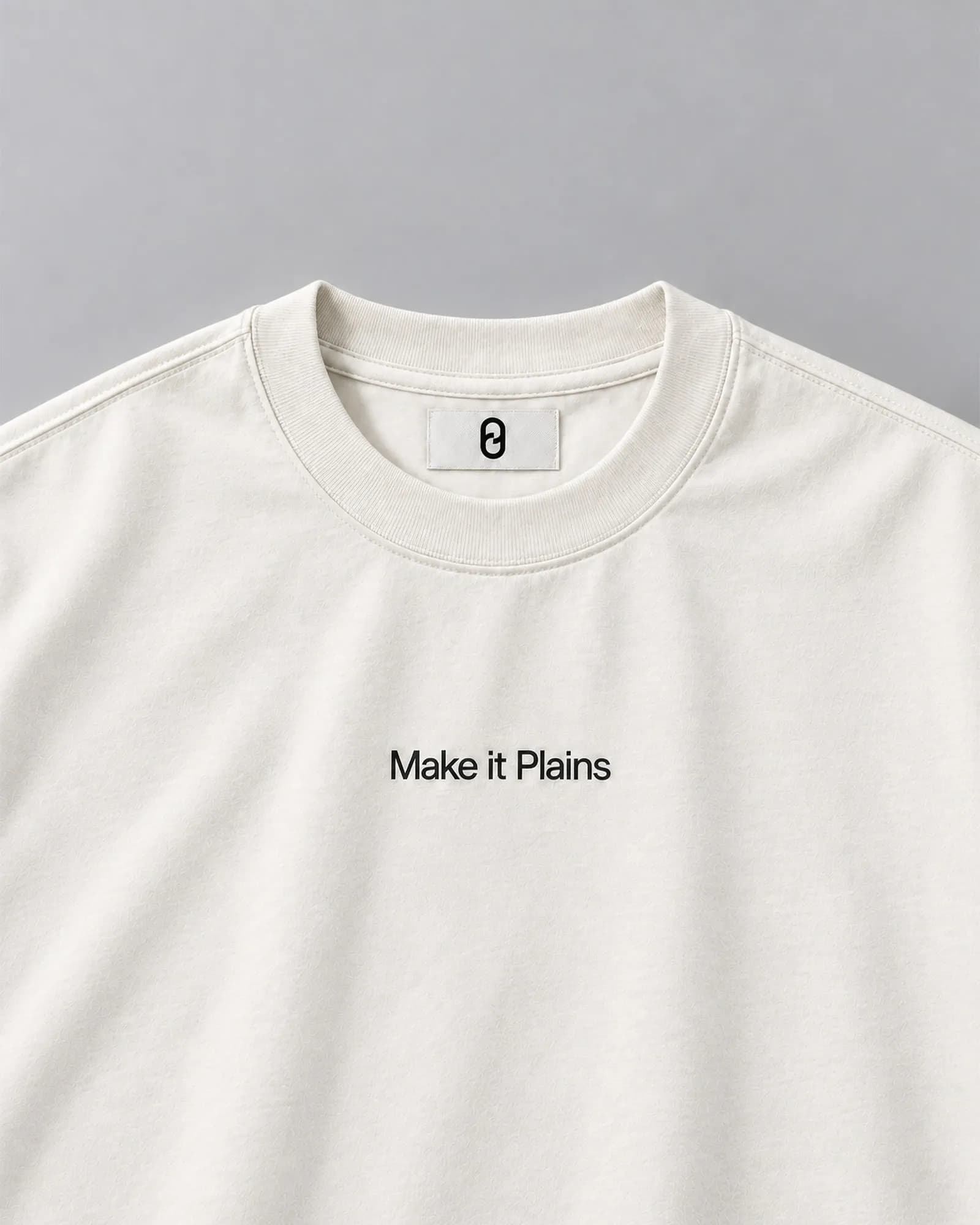 Off-white T-shirt on a blue-grey background with a small P/0 label at the neckline. The chest text reads "Make it Plains" in a single type size.