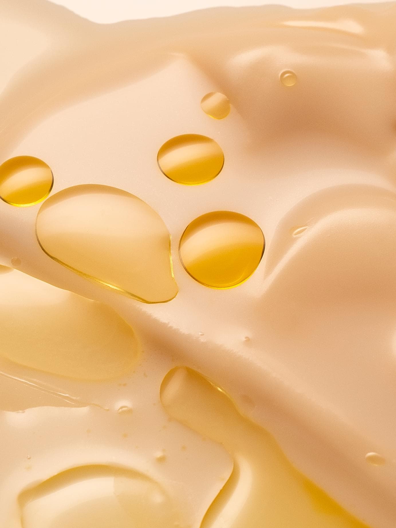 Close-up of a creamy skincare texture with golden oil droplets resting on the soft, off-white lotion.