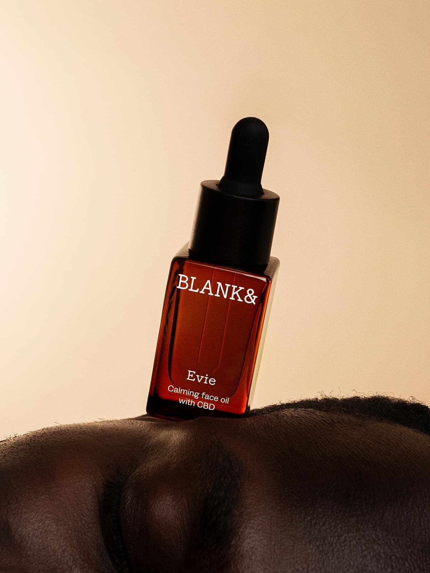 Blank& Evie bottle with black dropper cap balanced on a shoulder against a warm beige backdrop; the label reads 'Evie – Calming face oil with CBD'.