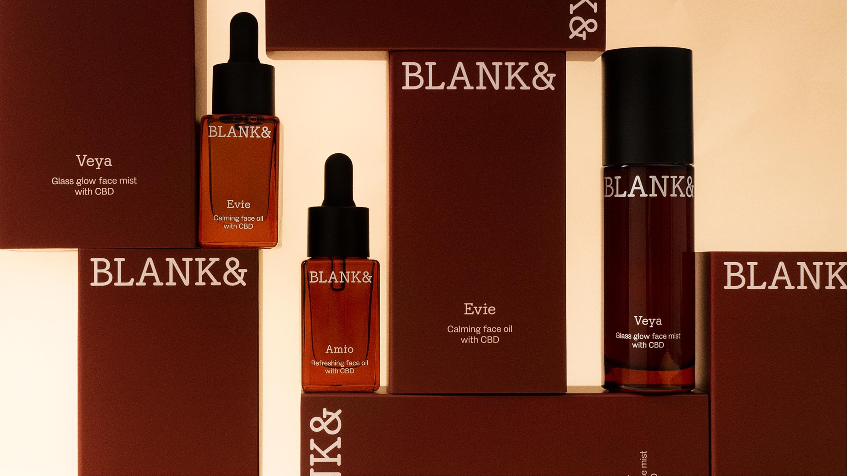 Full product lineup of the Blank& range: boxes and bottles for Veya, Evie and Amio arranged in layers against a warm background.